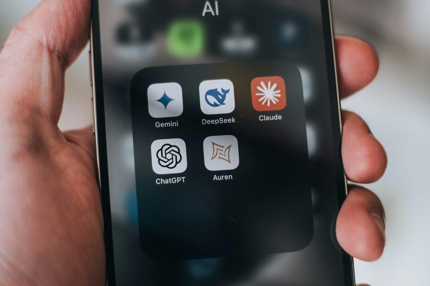 Smartphone met app-menu waarin verschillende AI-applicaties als Gemini, DeepSeek, Claude, ChatGPT en Aurgen zichtbaar zijn. Dit illustreert hoe AI-tools