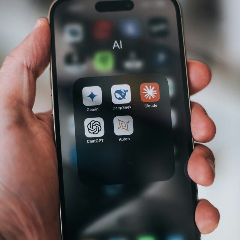 Smartphone met app-menu waarin verschillende AI-applicaties als Gemini, DeepSeek, Claude, ChatGPT en Aurgen zichtbaar zijn. Dit illustreert hoe AI-tools