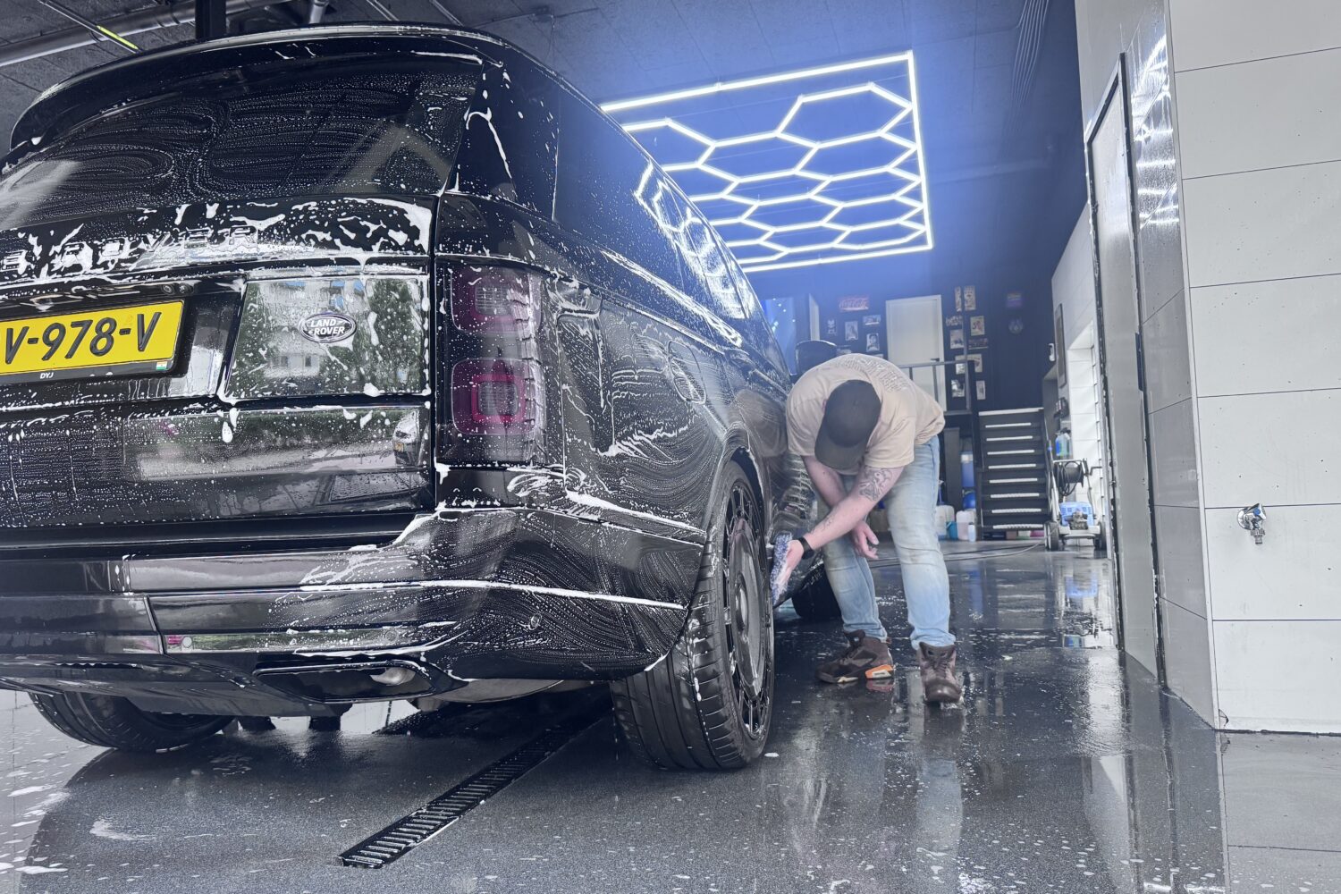 Een persoon wast de achterkant van een zwarte Range Rover met schuim in een автомий.
