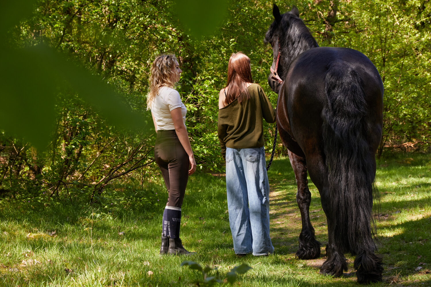 Twee vrouwen staan naast een zwarte paard op een grasveld.