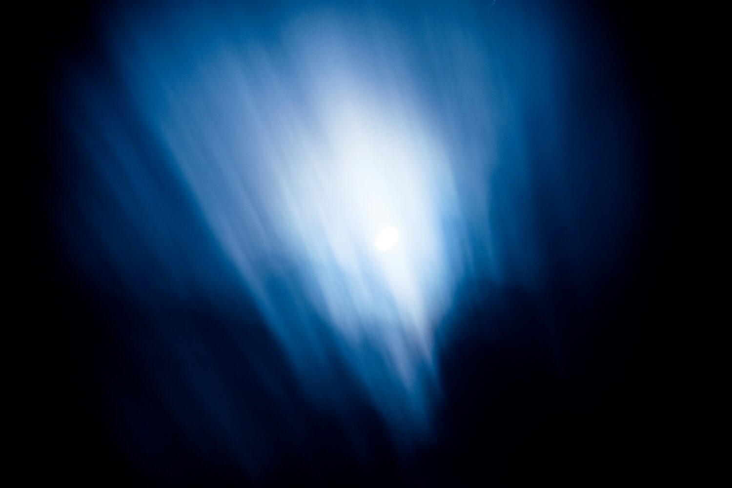 Een heldere, witte lichtbron schijnt in een donkere ruimte met blauwe lichtstrepen.