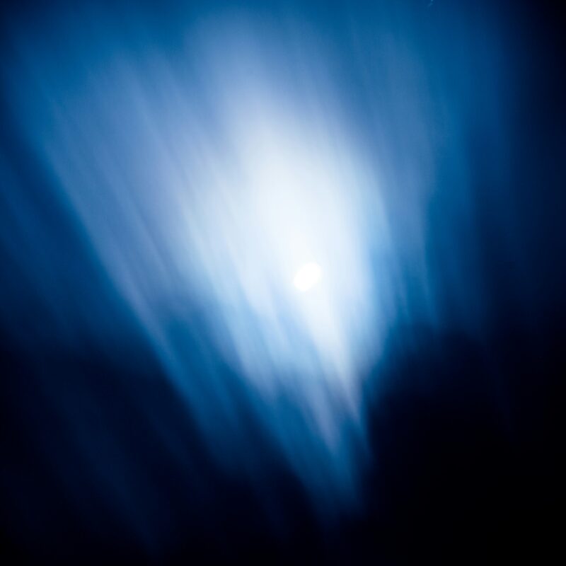 Een heldere, witte lichtbron schijnt in een donkere ruimte met blauwe lichtstrepen.